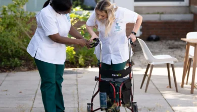 Occupational Therapy student with patient helping them walk with a frame outside