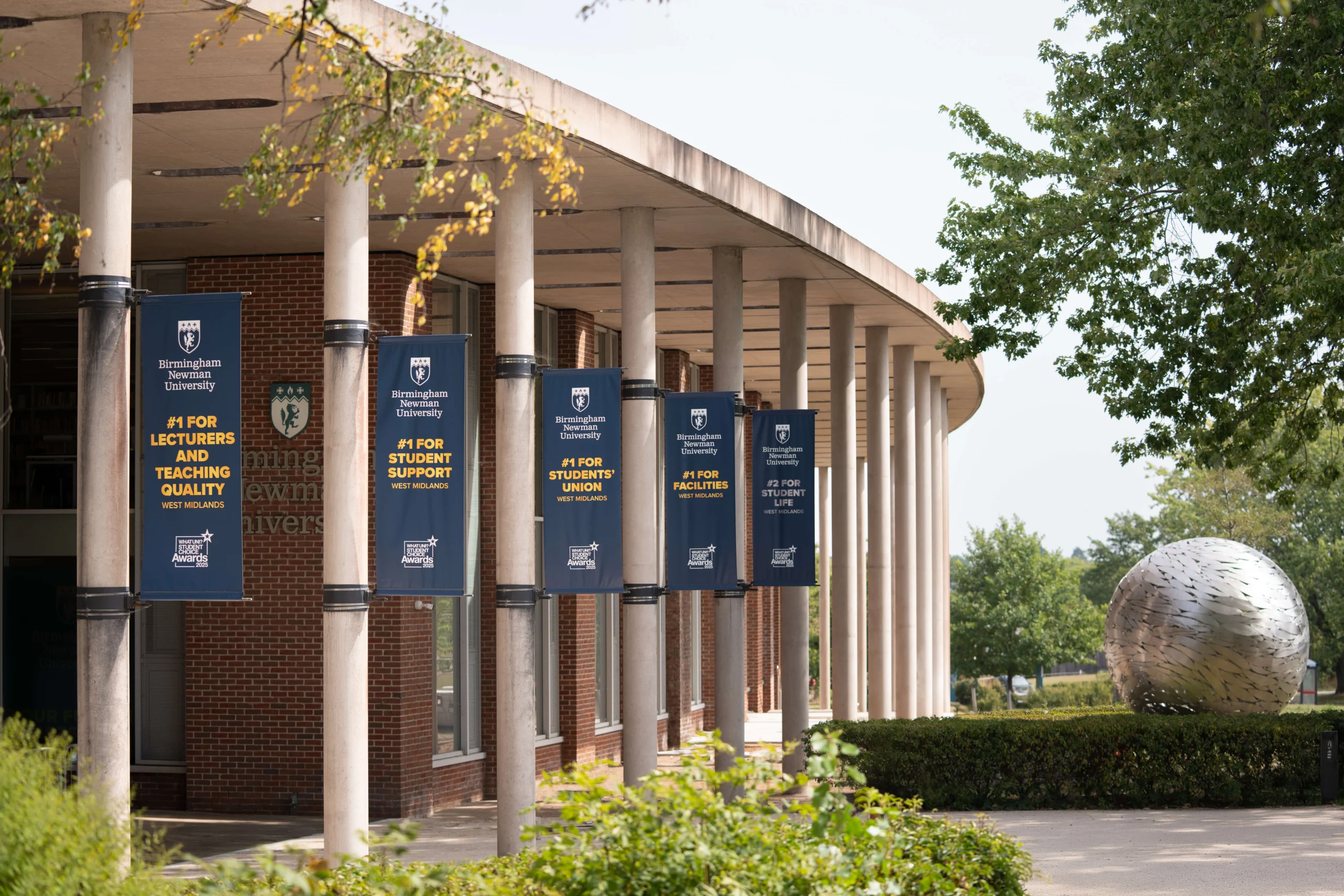 Birmingham Newman University front entrance with globe and awards on flags