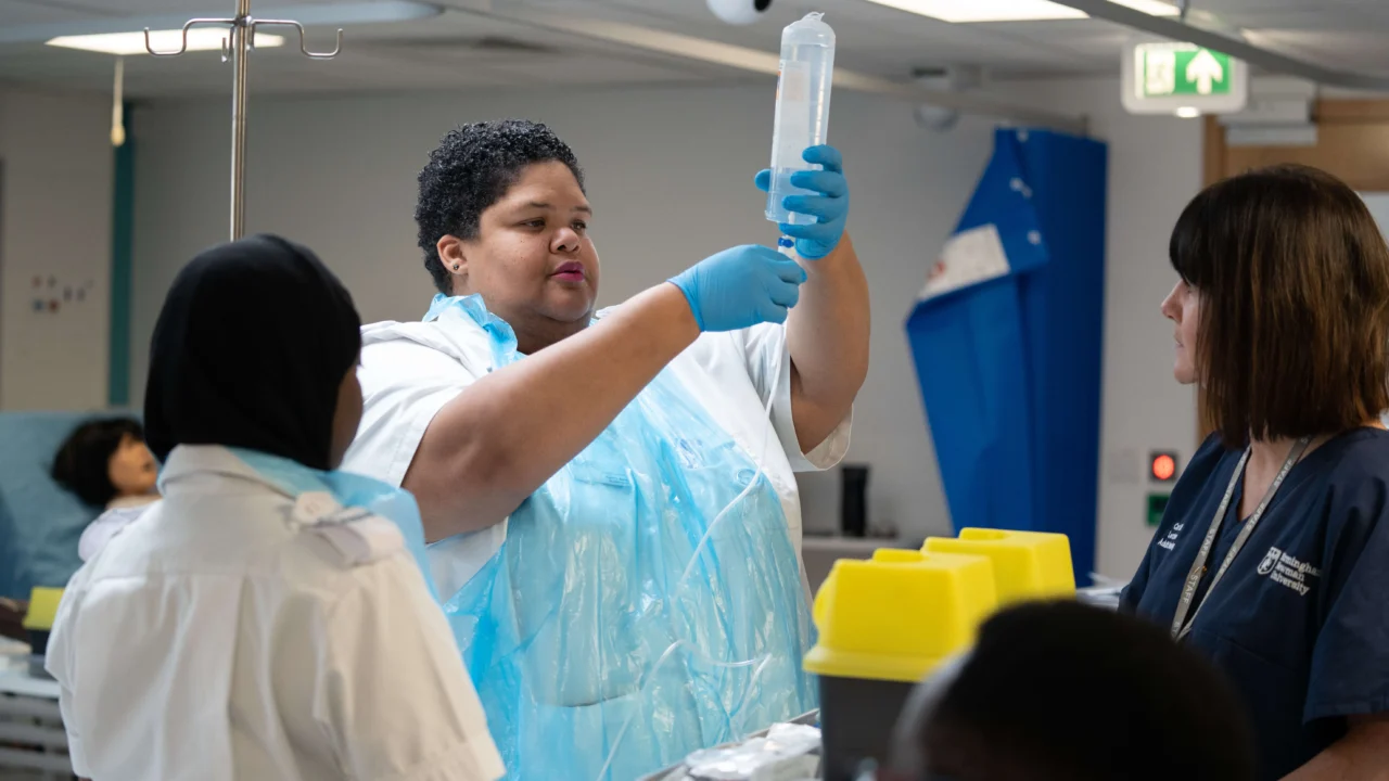 Adult Nursing MSc students in a bright, modern clinical skills lab practicing patient care techniques using hospital beds, medical equipment, and simulation mannequins, with instructors providing guidance.