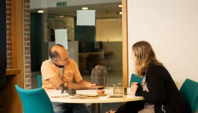 history student with short brown hair wearing a dark sweater, sitting at a wooden desk in a bright university library, deeply focused on reading an open book while researching historical topics, with shelves of historical texts in the background.