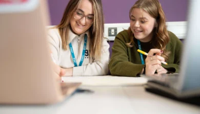 Education students in class talking at table with laptop