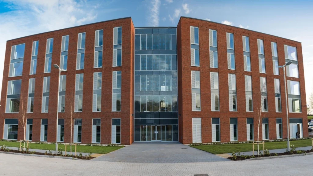Exterior view of Cofton Hall at Birmingham Newman University, showing a modern brick building with large windows and landscaped surroundings