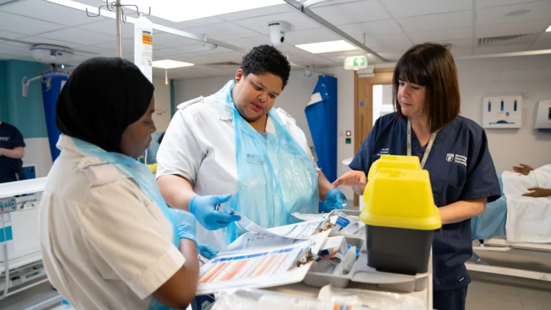 Students nurses in training ward being being shown information on clipboard