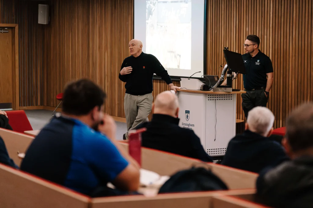 Les Cusworth, former England rugby player and coach, smiling in front of a neutral background, wearing a dark jacket and light shirt.