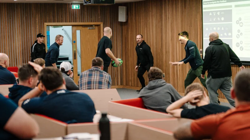 Rugby coaching event organized by North Midlands RFU, showing coaches demonstrating tackling drills and passing techniques to players