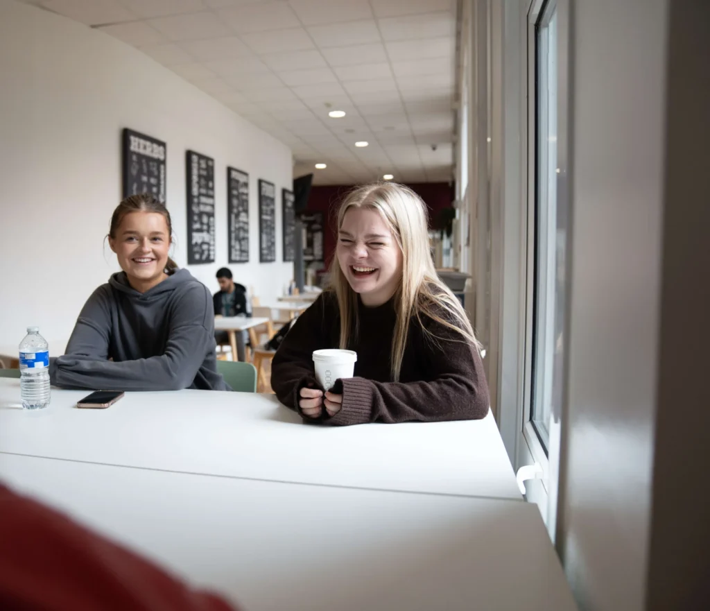 Students sitting and chatting in Bistro32 at Birmingham Newman University, with a bright, modern interior and casual dining atmosphere.