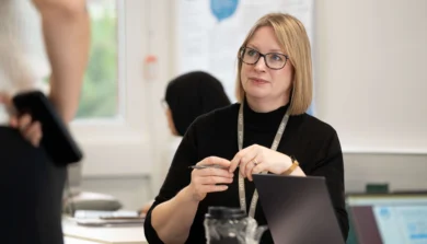 Students engaged in a classroom session, seated in a bright, modern classroom with natural light and discussion materials on the table